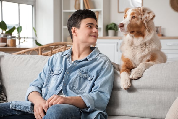 Teenage boy sitting on the sofa looking at a dog sitting next to him.