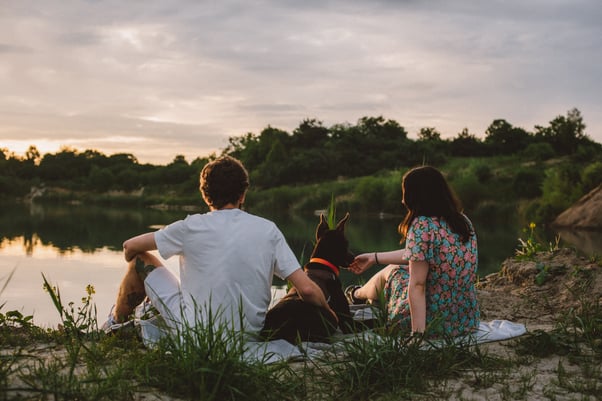 Two people sitting by a lake with their dog.