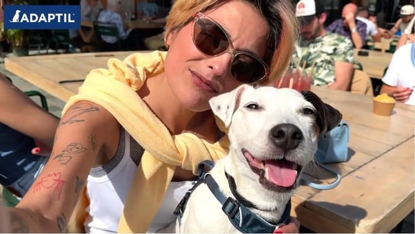 Dog and their human looking into the camera while sitting at a table with friends. The dog is wearing an ADAPTIL Calm Collar.