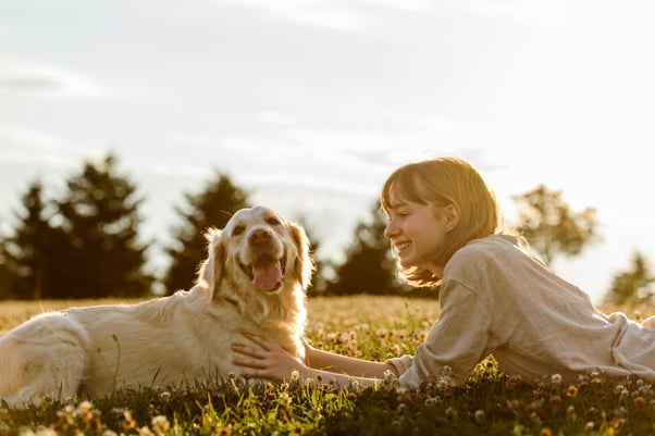 Woman lying with her dog on a grassy field