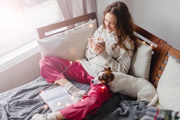 Small dog resting on a woman’s lap on a bed.