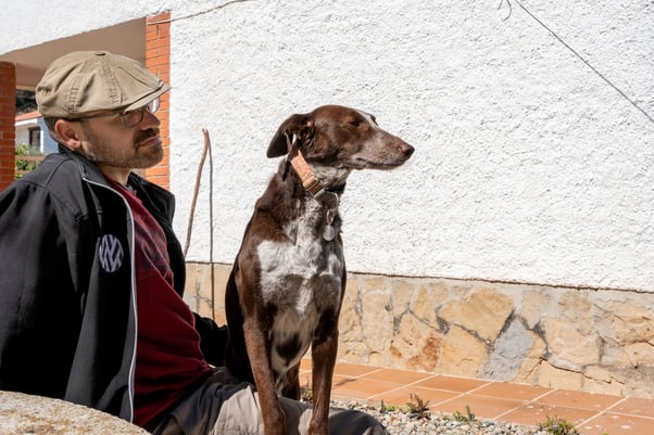 Man sitting outside wearing a brown hat with a brown dog on his lap.
