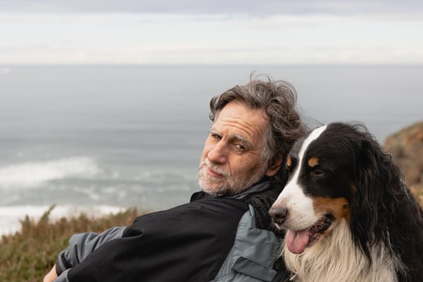 Older man sitting with his dog overlooking the sea.