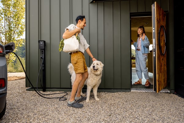 Woman standing in a doorway greeting a man and dog.