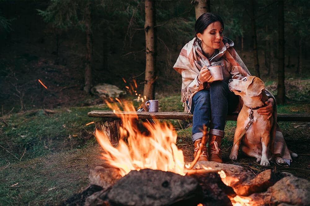 Frau und Hund am Lagerfeuer beim Campen