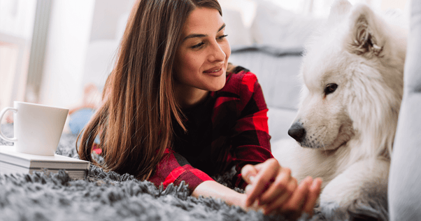 Young woman laying on carpet looking lovingly at large fluffy white dog