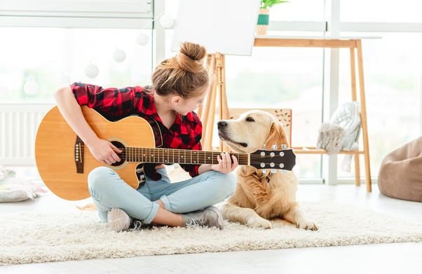 Girl playing guitar and singing to her dog. 